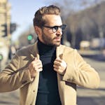 Fashionable young man with sunglasses poses outdoors in a sunny Budapest street scene.
